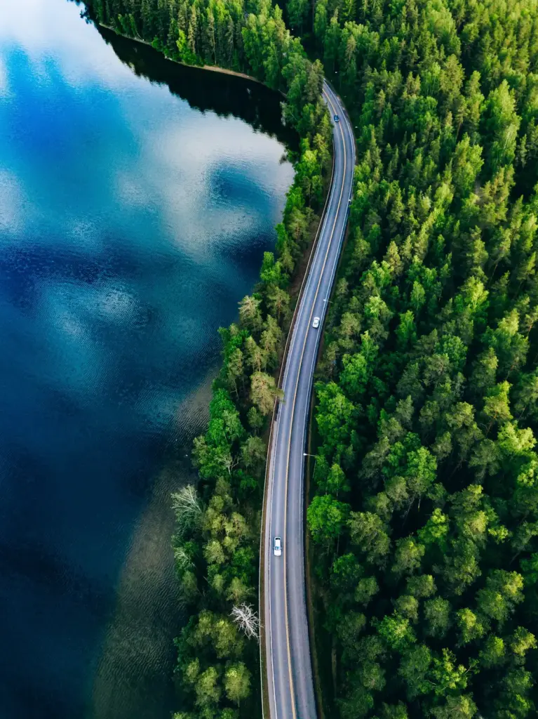 The Road Ahead 1 Aerial view of a road winding through a green pine forest beside a deep blue lake